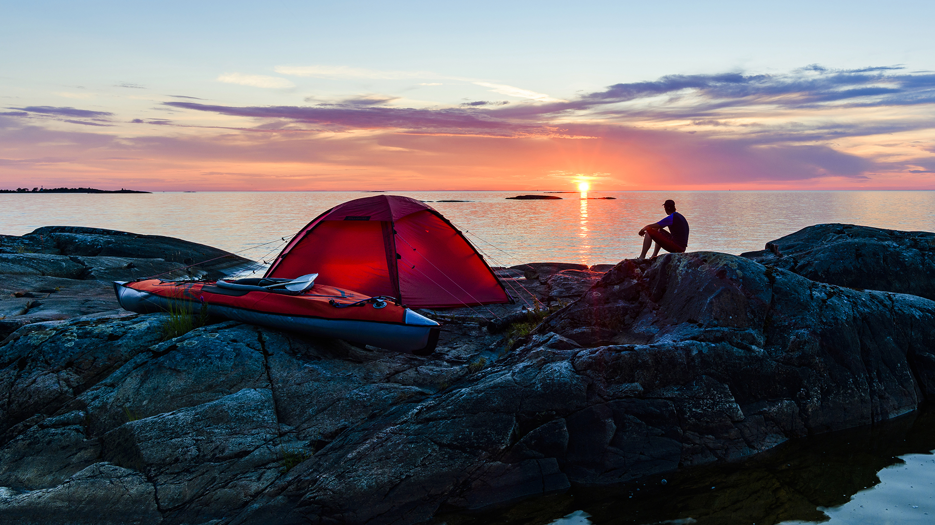 Man sitter vid upplyst tält vid Vänern (Ekens skärgård).